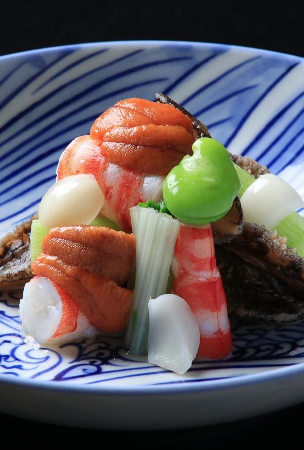 縞模様の美しい和食器に盛り付けられた、色鮮やかな海の幸と野菜の和え物。ウニやエビ、アワビのような貝類、そして緑色の豆や白い野菜がバランスよく配され、素材の新鮮さと彩りが際立っています。